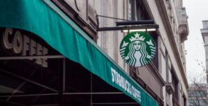 El icónico logo circular verde de la sirena de Starbucks colgado sobre un toldo de color verde turquesa en la fachada de un edificio urbano de estilo clásico. Cada vez hay mas en Mexico