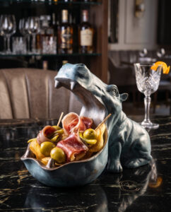 Tapa de jamón ibérico, aceitunas y gildas servida en una original escultura de hipopótamo sobre barra de mármol negro en Mala Yegua Santander.